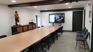 Une salle de conférence avec une longue table, des chaises, une statue, un écran de projection et une porte.