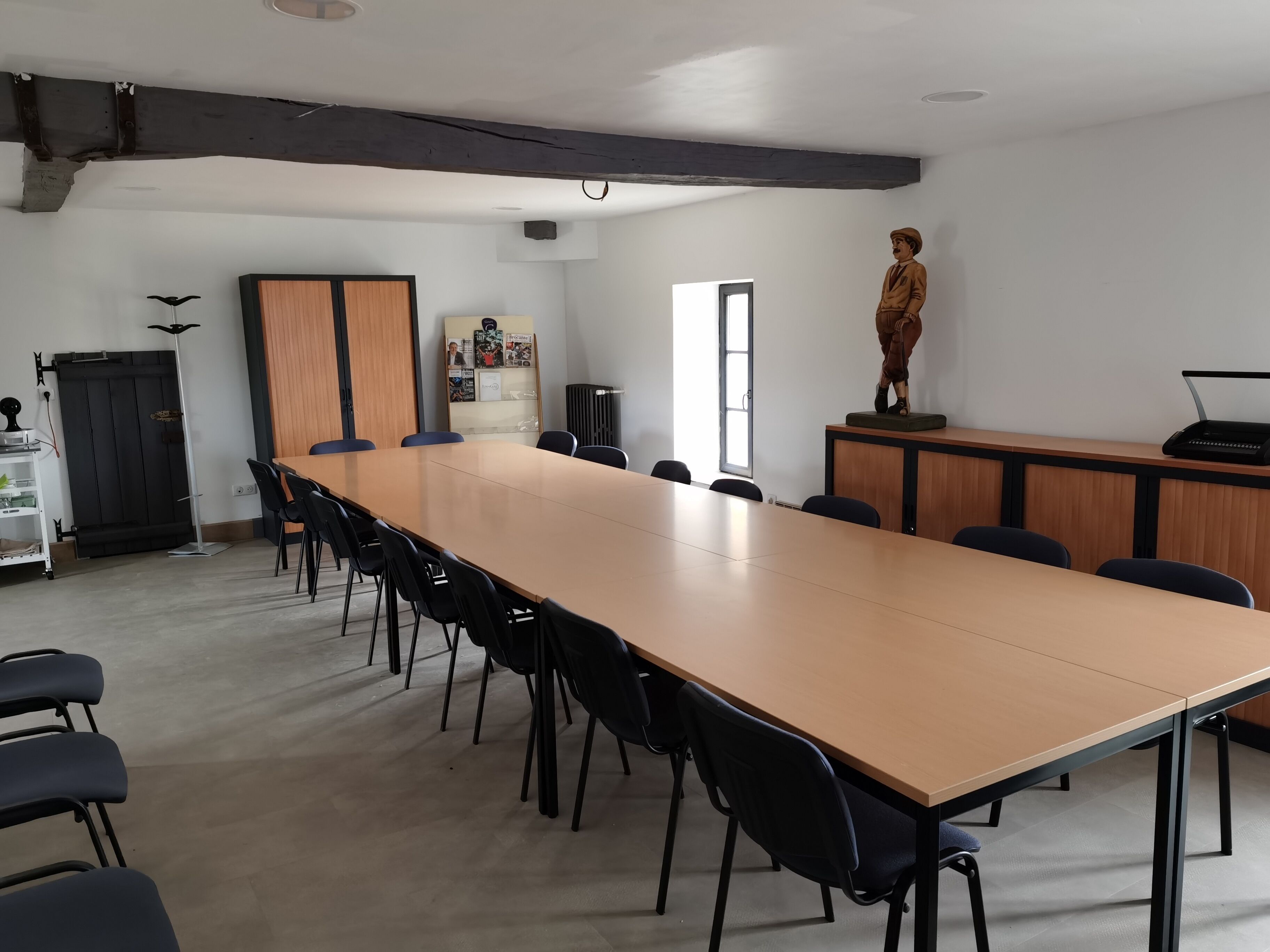 A conference room with a long table, black chairs, a wooden cabinet, a statue, and a window.