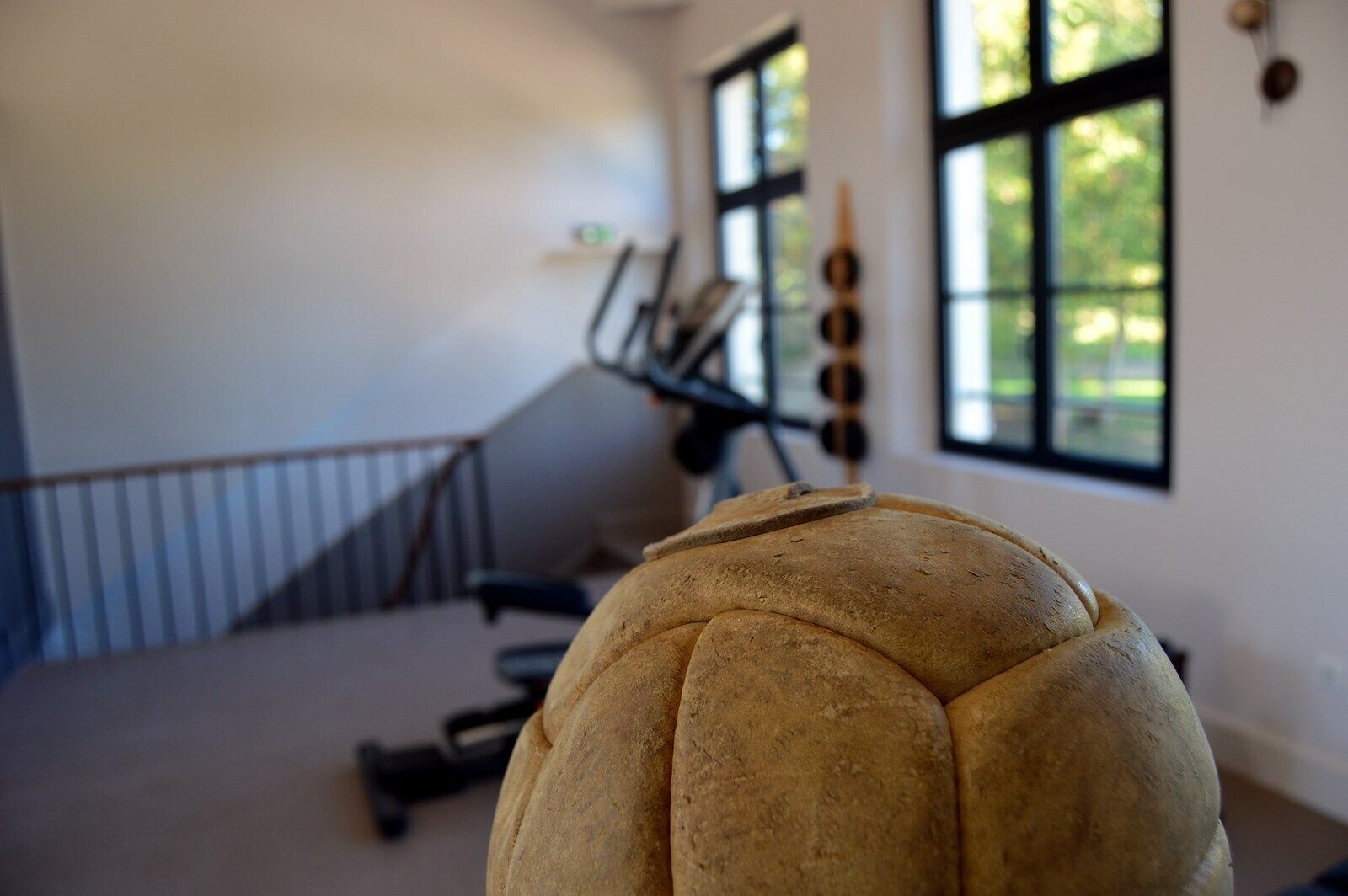 A room with a large, round, textured object in the foreground, a staircase, and a window with a view of greenery.