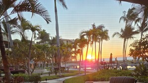 Un patio con una mesa redonda y sillas, palmeras y vista al atardecer.