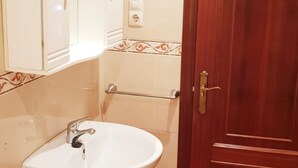 A bathroom with a white pedestal sink, a wooden door, and a mirror above the sink. - Apartamento Playa da Ribeira Finisterre (Fisterra)
