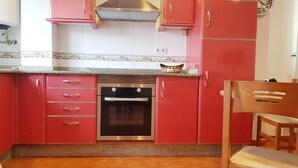 A kitchen with red cabinets, a stainless steel oven, and a tiled backsplash. - Apartamento Playa da Ribeira Finisterre (Fisterra)