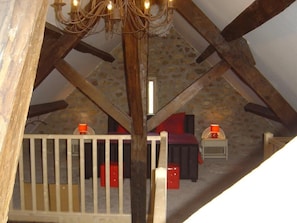 Une pièce dotée d’un plafond en pente, de poutres apparentes, d’une rambarde blanche et d’un lustre.