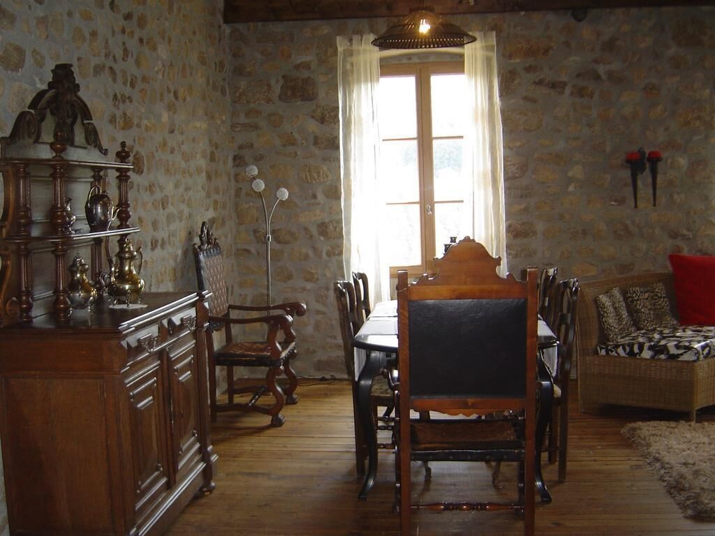 Un'area pranzo con un tavolo e sedie in legno, una parete in pietra e una finestra con tende.