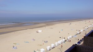 Une plage avec un rivage sablonneux, quelques parasols et un voilier à l’horizon.