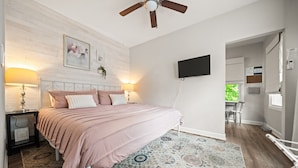 Un dormitorio con cama, lámparas de noche, ventilador de techo, televisor montado y alfombra estampada.