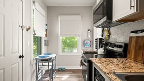 Una cocina con armarios blancos, encimera de granito, estufa y ventana.