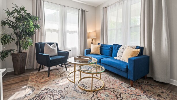 Una sala de estar con un sofá azul, un sillón azul oscuro, una mesa de centro redonda y una planta grande en maceta.