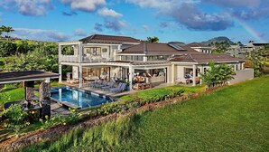 A large, two-story house with a swimming pool, multiple outdoor seating areas, and a lush garden. - Spectacular home with ocean and golf course views! (Koloa)