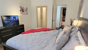 Une chambre à coucher comprenant un lit, une télévision, une armoire et une porte donnant sur une autre pièce.