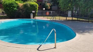 Une piscine avec un escalier en métal, entourée d’une clôture et d’arbres.