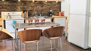 Une cuisine avec un mur recouvert de pierres apparentes, des meubles en bois, un réfrigérateur blanc et un coin bar avec des tabourets.
