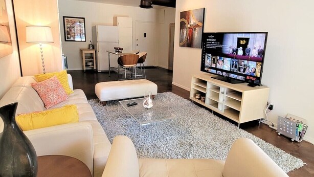 Un salon avec un canapé blanc, une table basse, un téléviseur posé sur un meuble et, au fond, un coin repas.