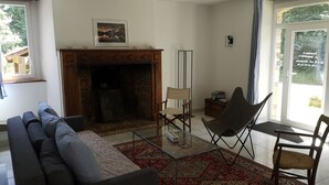A living room with a fireplace, a sofa, a glass coffee table, and two chairs. - Maison Cocoon en Brocéliande (Loutehel)