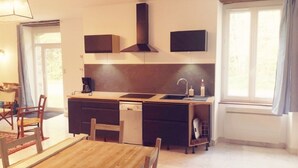 A compact kitchen with a central island, a built-in stove, and a microwave. There is a dining area with a wooden table and chairs. - Maison Cocoon en Brocéliande (Loutehel)