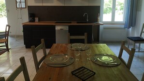 A modern kitchen with a central island, built-in dishwasher, and a window providing natural light. - Maison Cocoon en Brocéliande (Loutehel)