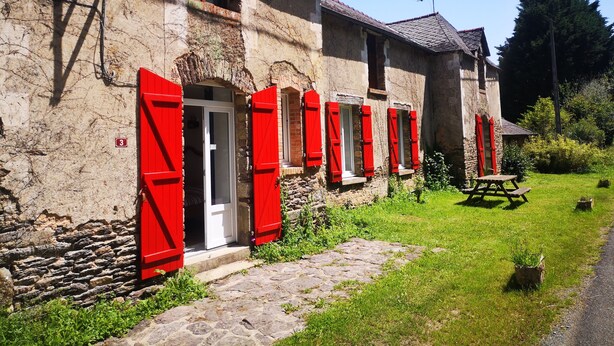A stone building with red shutters, a stone pathway, and a picnic table in a garden. - Maison Cocoon en Brocéliande (Loutehel)