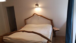 A wooden bed with a headboard, a bedside table, and a wall-mounted light fixture. - Maison Cocoon en Brocéliande (Loutehel)