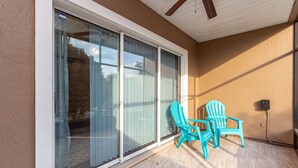A covered patio with sliding glass doors, a ceiling fan, and two turquoise chairs. - Central Jacksonville Location! (Jacksonville)