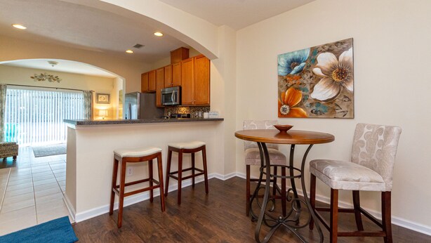 A modern kitchen with wooden cabinets, a microwave, and a dining area with a round table and bar stools. - Central Jacksonville Location! (Jacksonville)