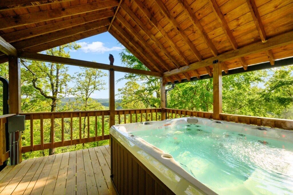 Een houten terras met een jacuzzi en uitzicht op bomen en heuvels.