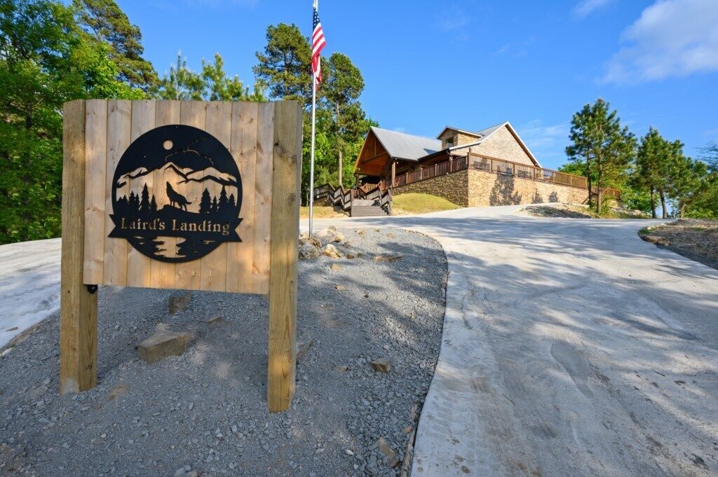 A wooden sign with a logo and the text "Laird's Landing" in front of a lodge with a stone facade and a wooden deck.