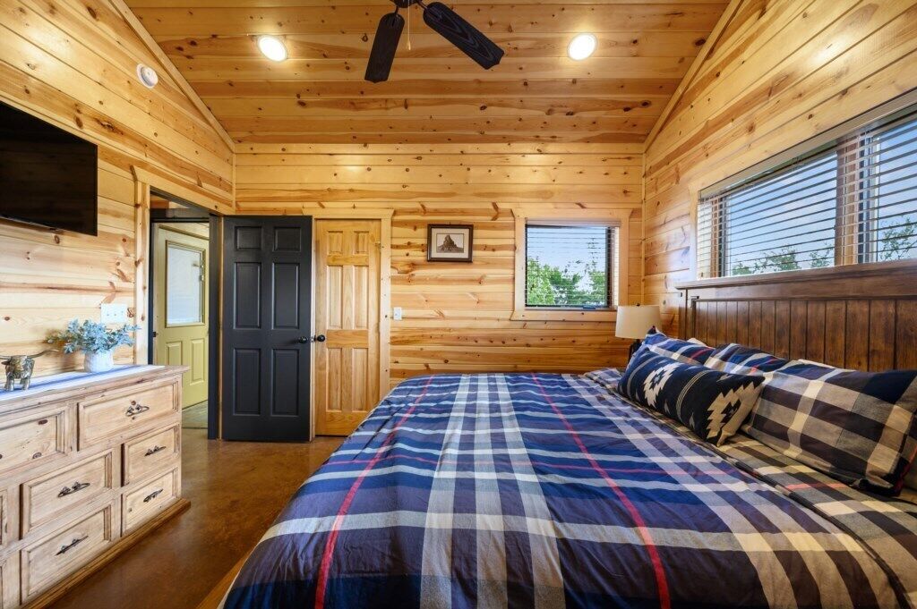 A wooden cabin bedroom with a bed, dresser, and a ceiling fan.