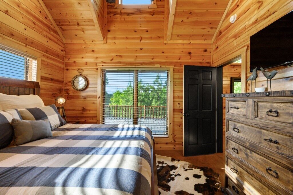 Un dormitorio de cabaña de madera con cama, cómoda y ventana con vista a follaje.