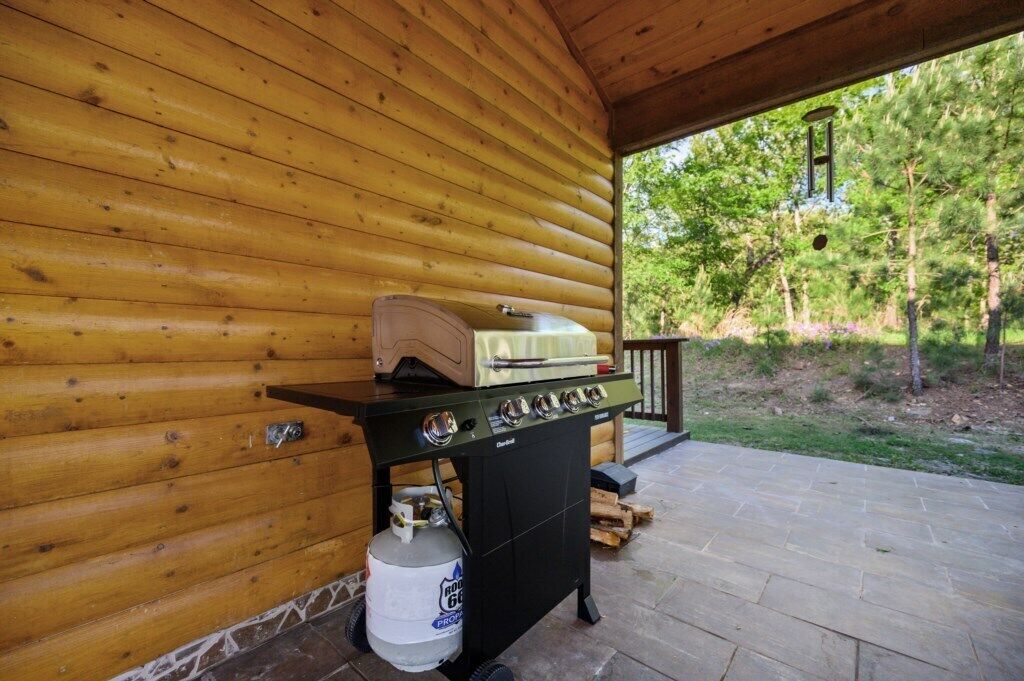 A wooden cabin with a barbecue grill and propane tank on the porch.