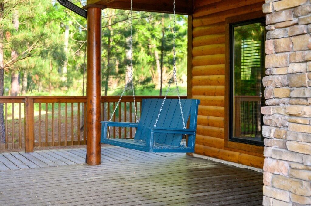 Una terraza de madera con una silla mecedora, un muro de piedra y una ventana con vistas a un bosque.