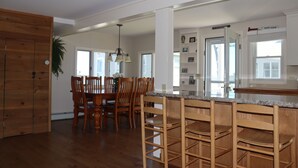 A spacious kitchen with wooden cabinets, a dining area with a wooden table and chairs, and a bar area with a granite countertop. - One of kind Ocean Front Compound with private beach! (Biddeford)