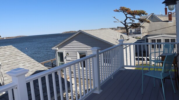 A deck with a railing overlooking a body of water, a small shed, and a dining area with chairs. - One of kind Ocean Front Compound with private beach! (Biddeford)