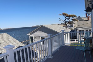 A deck with a railing overlooking a body of water, a small shed, and a dining area with chairs. - One of kind Ocean Front Compound with private beach! (Biddeford)