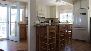 A kitchen with wooden cabinets, a white refrigerator, and a bar area with stools. - One of kind Ocean Front Compound with private beach! (Biddeford)