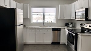 Una cocina moderna con armarios blancos, lavavajillas de acero inoxidable, refrigerador negro, microondas y horno.