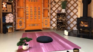 Una habitación acogedora con una puerta de madera grande, un pequeño estante de madera con una planta, una estufa negra y una colchoneta de yoga.