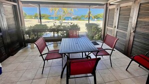 An outdoor patio with a table and chairs, a view of the beach, and a covered area with shutters. - Lux King Suite On Sand @ Sapphire Beach Resort II (St Thomas)