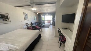 A hotel room with a bed, a desk with a chair, a television, and a view of the outside. - Lux King Suite On Sand @ Sapphire Beach Resort II (St Thomas)