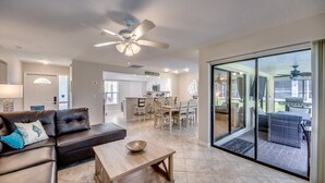 A spacious living area with a leather sofa, a wooden coffee table, and a ceiling fan. A glass door leads to a patio with outdoor furniture. - Newly Renovated! Prime Location! Premium bedding! Heated Pool! 3 Br/ 2 Bath (Cape Coral)
