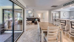 A spacious living area with a large wooden dining table, comfortable seating, and a view through glass doors. - Newly Renovated! Prime Location! Premium bedding! Heated Pool! 3 Br/ 2 Bath (Cape Coral)