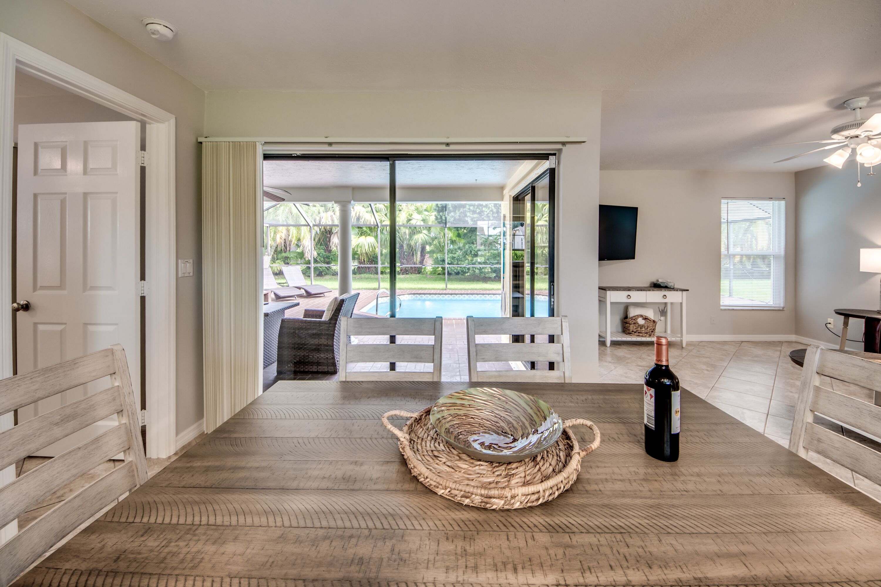 Ein geräumiges Zimmer mit Holzboden, großem Fenster und Blick auf einen Pool. Auf dem Tisch steht eine Weinflasche.