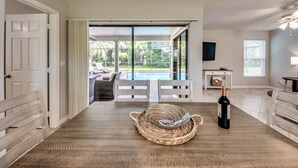 A spacious room with a wooden floor, a large window, a pool view, and a bottle of wine on the table. - Newly Renovated! Prime Location! Premium bedding! Heated Pool! 3 Br/ 2 Bath (Cape Coral)