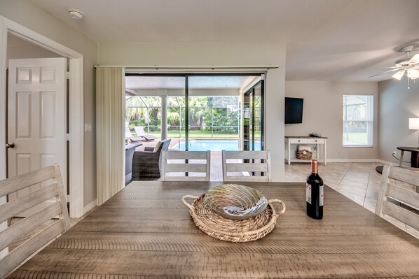 A spacious room with a wooden floor, a large window, a pool view, and a bottle of wine on the table.