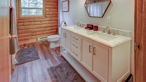 Une salle de bain avec des murs en bois, des toilettes blanches, un meuble-lavabo avec un plan de travail en marbre et un miroir.