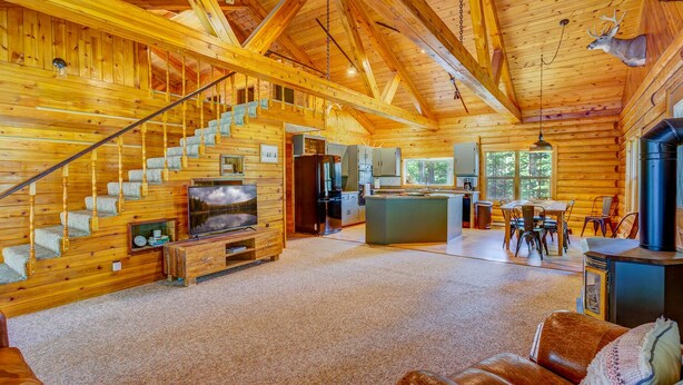 L’intérieur d’une cabane en rondins comprend un escalier, une cuisine, un coin repas et un salon avec une cheminée.
