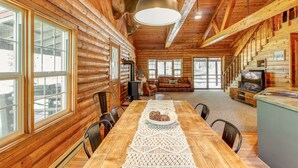 L’intérieur d’une cabane en rondins, avec une table à manger, des chaises, un canapé, une cheminée et un téléviseur.