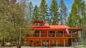 Une cabane en rondins à deux étages, avec un toit rouge, une véranda et un drapeau américain.
