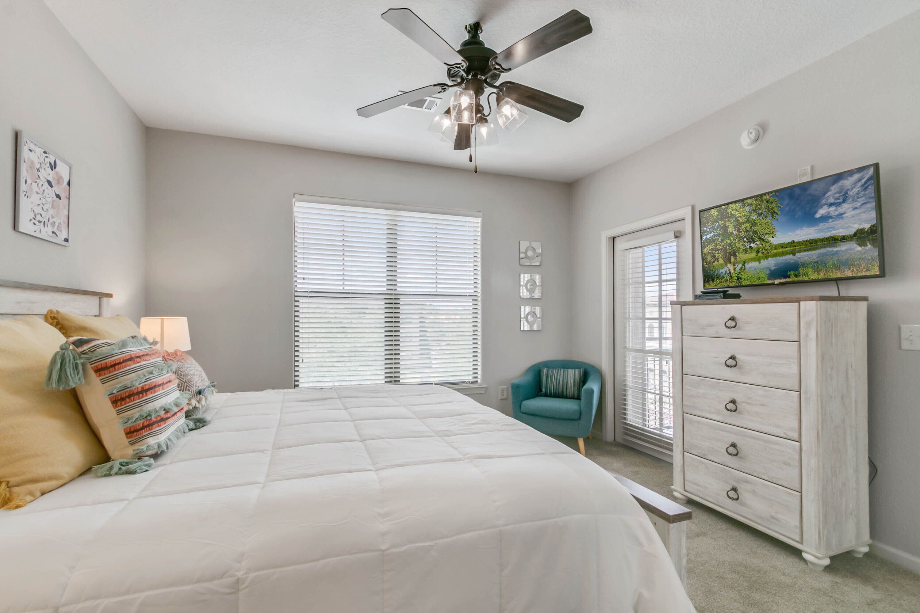 A bedroom with a bed, a ceiling fan, a dresser, a chair, and a TV on the wall.
