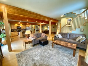 Relax in this airy living space with a high ceiling and exposed beams, featuring a sofa, coffee table, and staircase leading to an upper level.