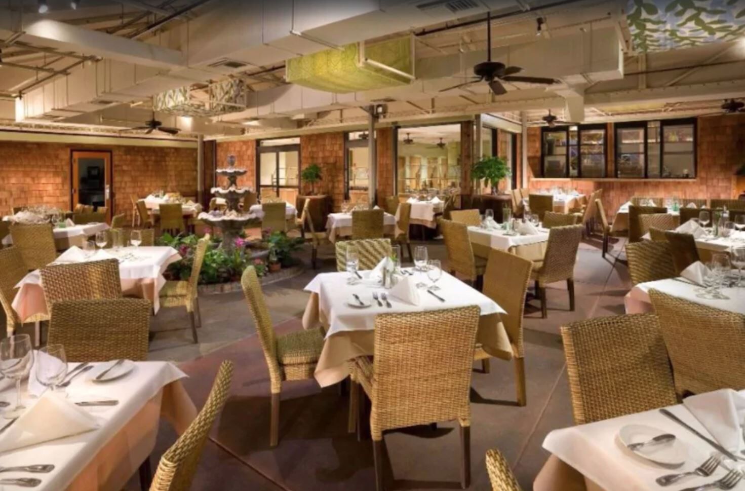 Un restaurant avec de nombreuses tables et chaises, certaines recouvertes de nappes blanches et d’autres non.